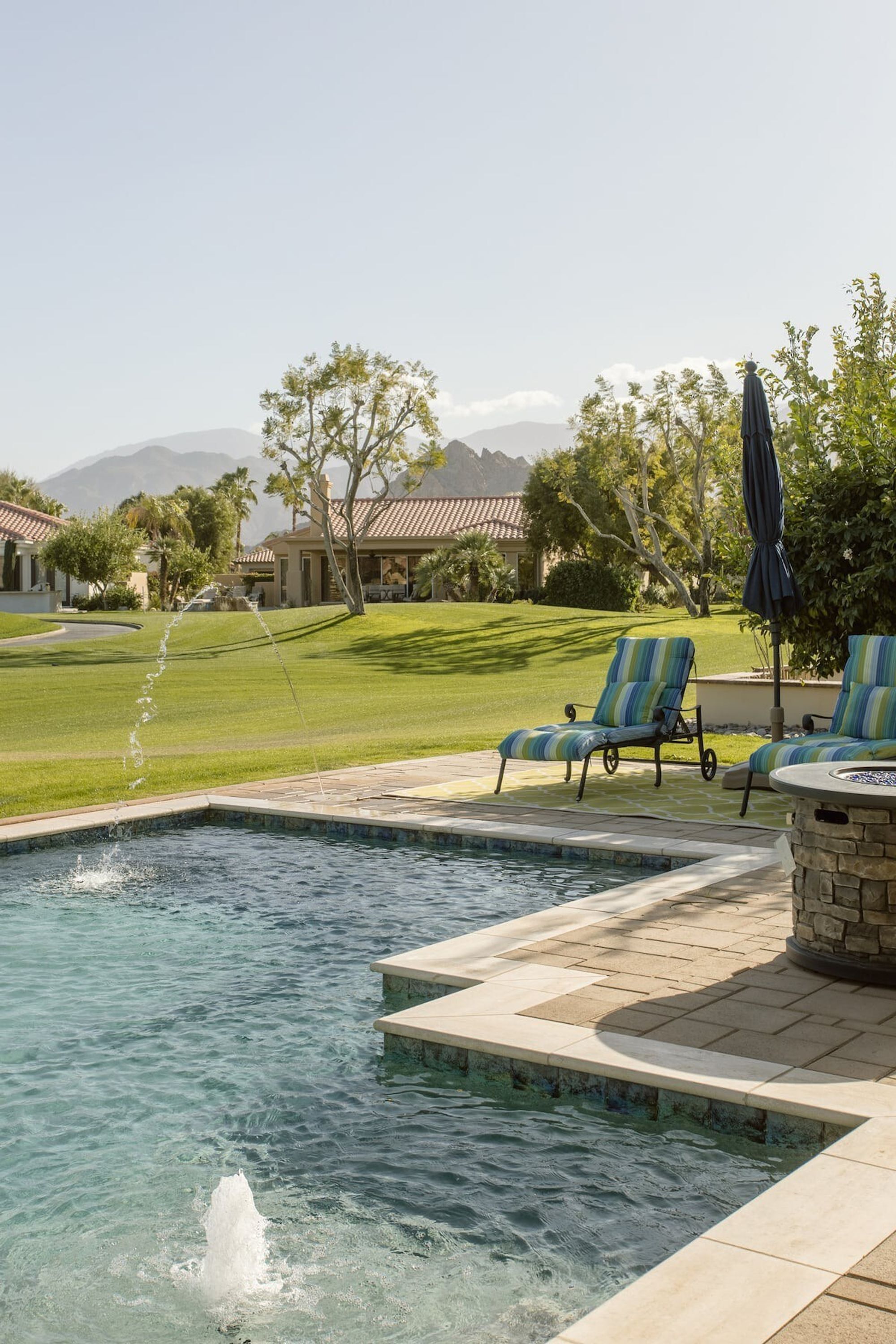 A swimming pool with a water feature, lounge chairs, and a stone wall.