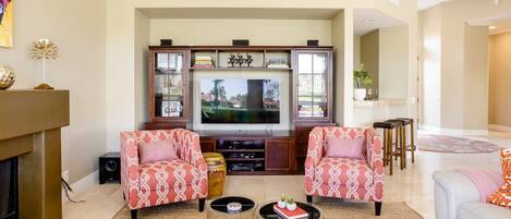 A living room with a fireplace, two patterned armchairs, a television, and a coffee table.