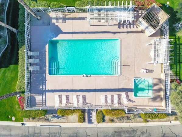 An aerial view of a swimming pool area with a rectangular pool, multiple lounge chairs, and a small hot tub. - Charming Condo With Golf Course View (Palm Desert)