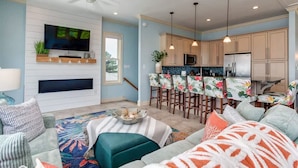A modern living room with a TV, seating area, and a kitchen with bar stools.