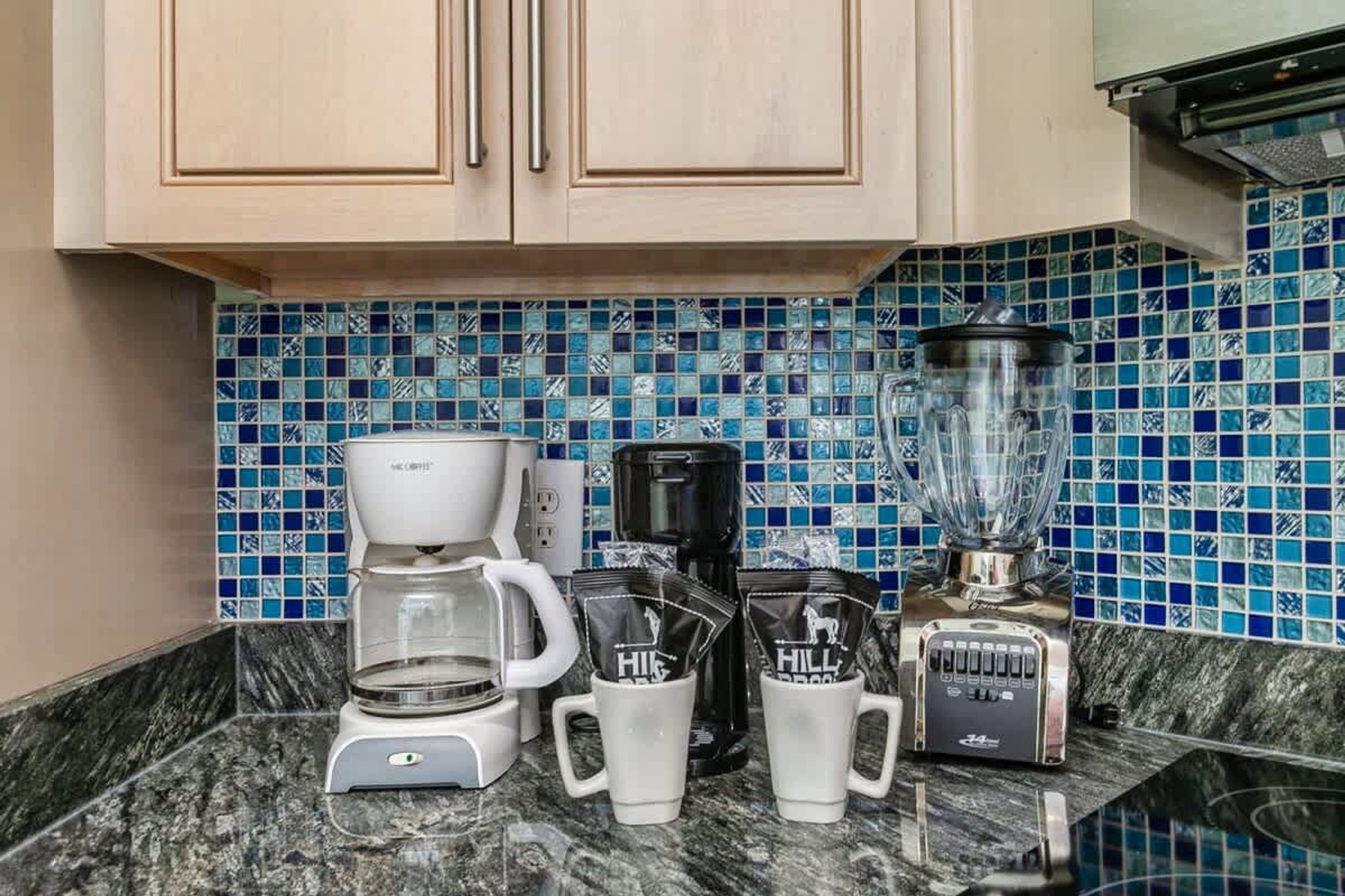 Een keuken met een koffiezetapparaat, een blender en twee mokken op het aanrecht.