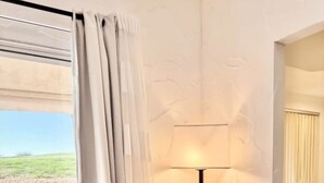 A modern room with a leather armchair, a floor lamp, and a view of a green landscape through a large window. - Fairway-view 3 Bedroom Condo in Palm Desert (Palm Desert)