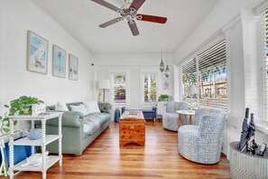 A spacious living room with a wooden coffee table, a sofa, and a chair. There are framed pictures on the wall and a ceiling fan. - Hibiscus House Bed Breakfast Citrus Room (Fort Myers)