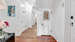 Un pasillo con paredes blancas, suelo de madera, una puerta con arco decorativo y un cuadro en la pared.