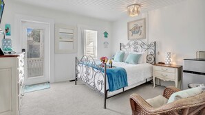 Un dormitorio con cama, cómoda, mesita de noche, silla de mimbre y ventilador de techo.