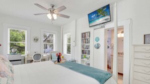 A bedroom with a bed, a desk, a bookshelf, and a TV on the wall. - Hibiscus House Bed Breakfast Seashell Room (Fort Myers)