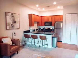 A modern kitchen with wooden cabinets, a stainless steel refrigerator, and a bar area with stools. - Downtown La Quinta Charmer- Walk to Dining Shops (La Quinta)