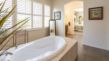 A spacious bathroom with a large bathtub, a walk-in shower, and a window with blinds.