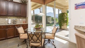 A modern kitchen with dark wood cabinets, a granite countertop, and a glass dining table with four chairs. - 5 Star Rating Oasis Golf Pool Spa 3bed Pga West (La Quinta)