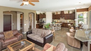 A spacious living room with a large sofa, a coffee table, and a kitchen area with dark wooden cabinets and a granite countertop. - 5 Star Rating Oasis Golf Pool Spa 3bed Pga West (La Quinta)
