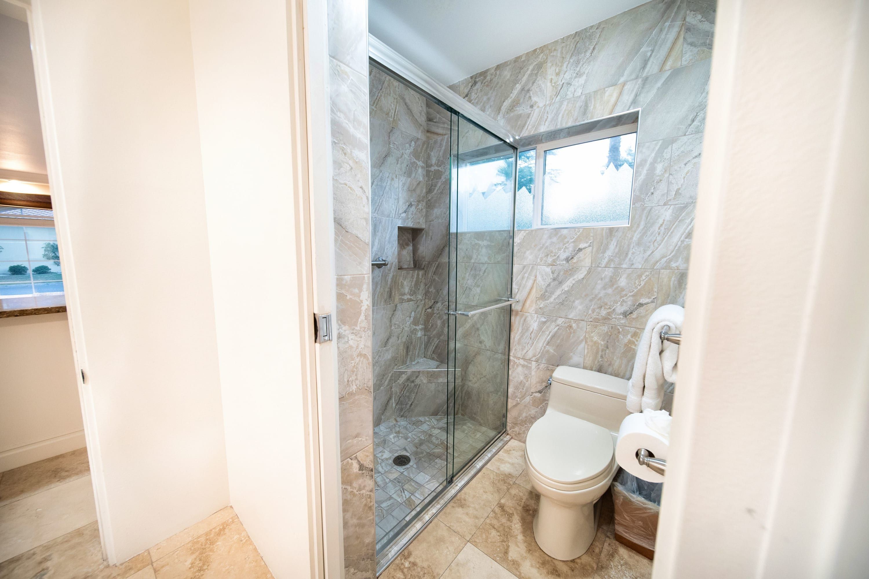 A modern bathroom with a glass-enclosed shower, a toilet, and marble walls.