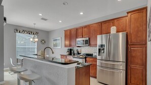 A modern kitchen with wooden cabinets, stainless steel appliances, and a central island. - Jedi Training Camp Top Rated 5 Star Villa (Kissimmee)