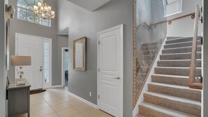 A hallway with a staircase, a chandelier, and a door with a mirror. - Jedi Training Camp Top Rated 5 Star Villa (Kissimmee)