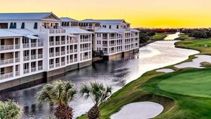 Un hotel con varios pisos, un río a su lado y un campo de golf al fondo.