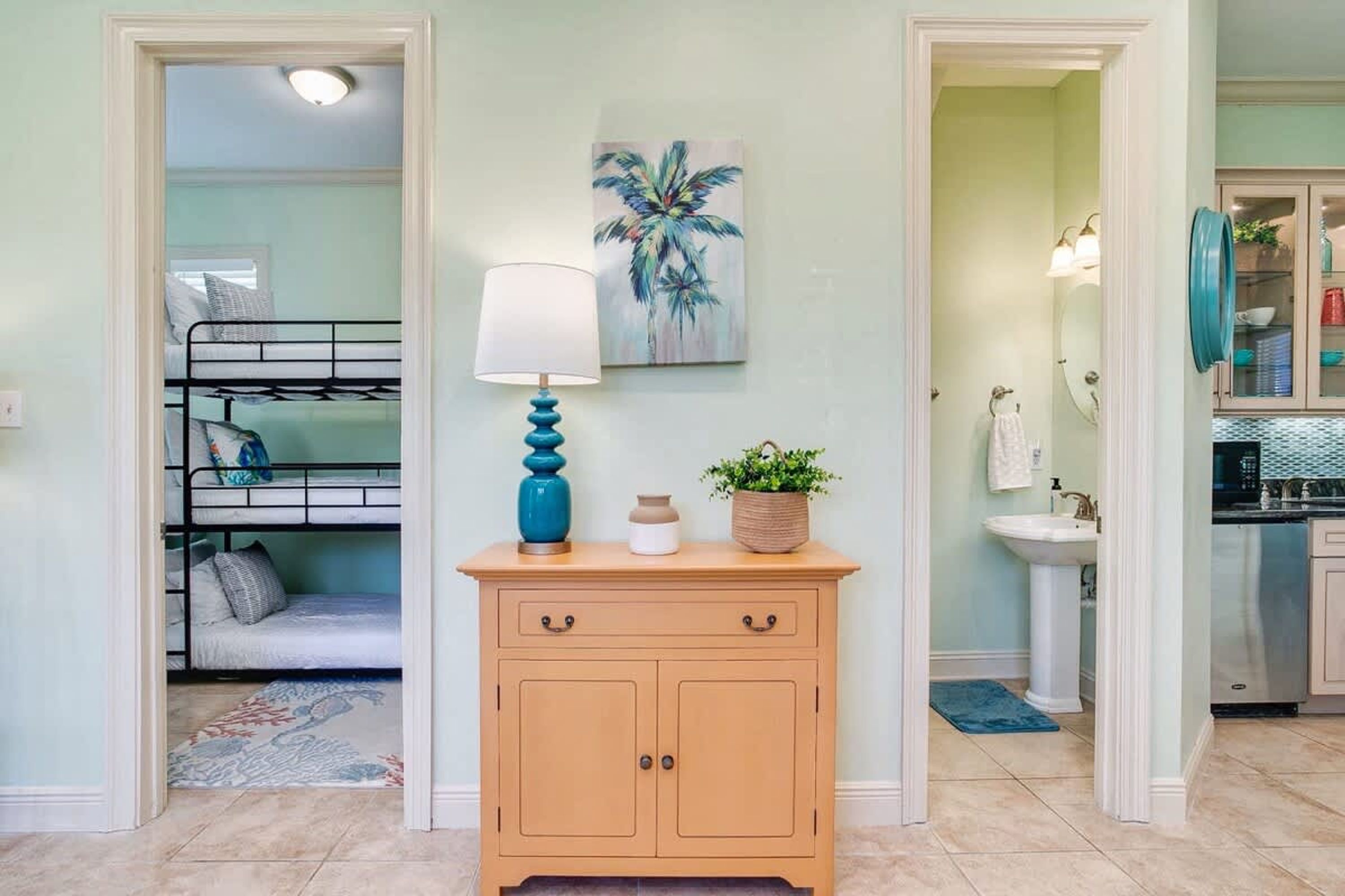 Una habitación con una cama litera, un armario de madera con cajones, una lámpara, un cuadro y un baño visible a través de una puerta abierta.