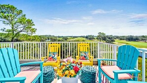 Una terraza con dos sillas Adirondack amarillas y una planta en maceta, con vistas a un campo de golf.