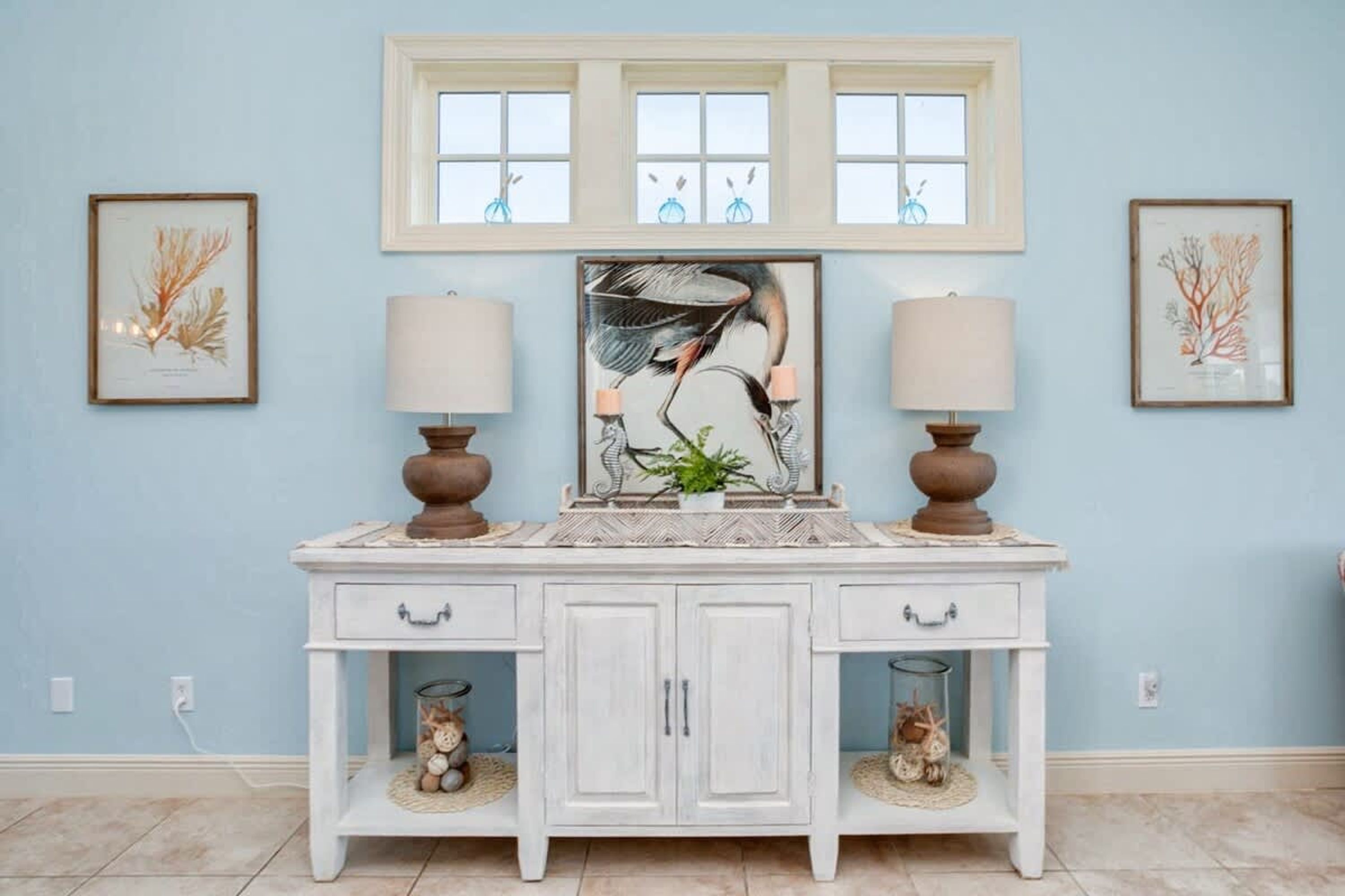 Una consola blanca con dos lámparas, una obra de arte enmarcada y dos pequeños frascos decorativos.