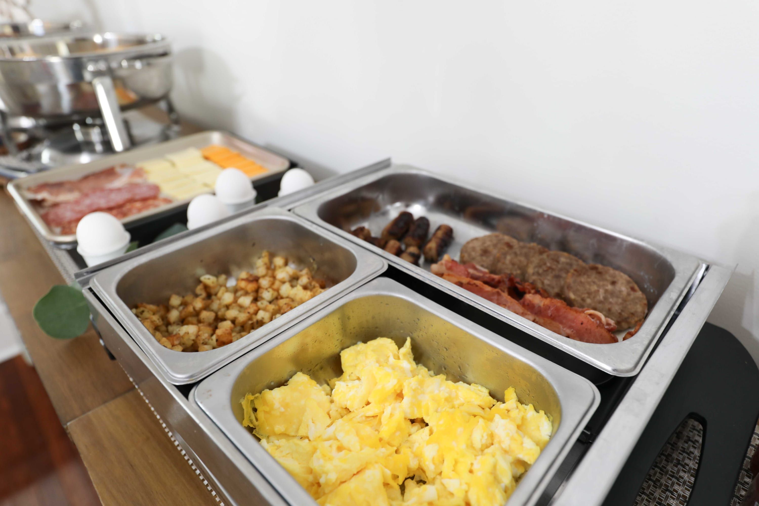 A buffet with various food items including scrambled eggs, sausages, bacon, and other breakfast foods.