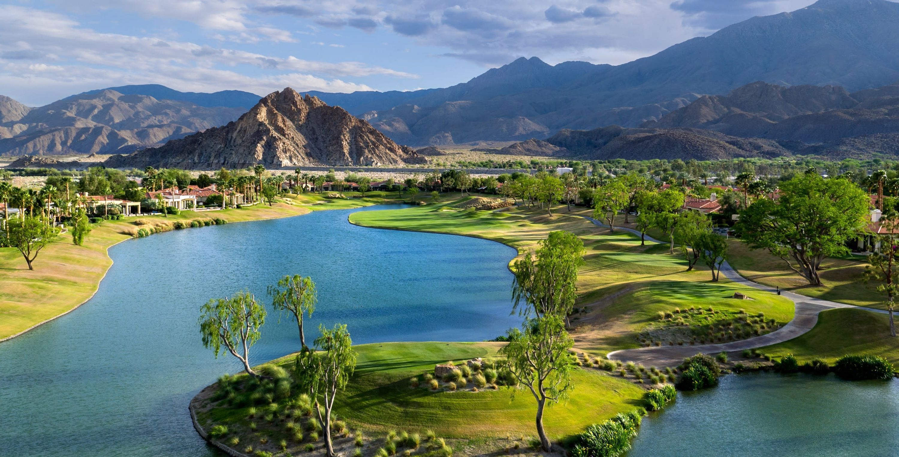 A golf course with a lake, mountains in the background, and a clear sky.