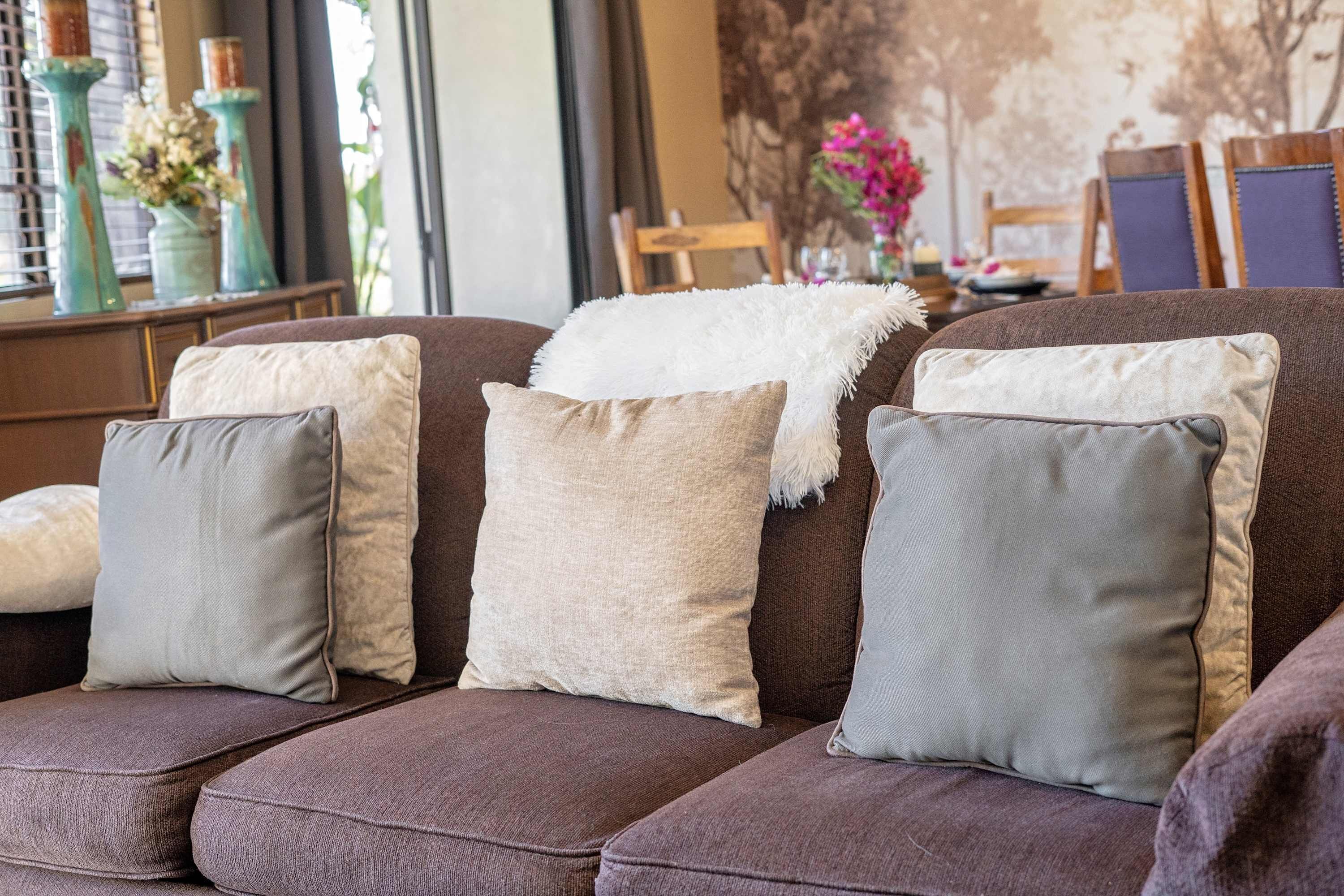 Ein braunes Sofa mit drei Kissen, einer weißen Tagesdecke und einer Blumenvase auf einem Holztisch.