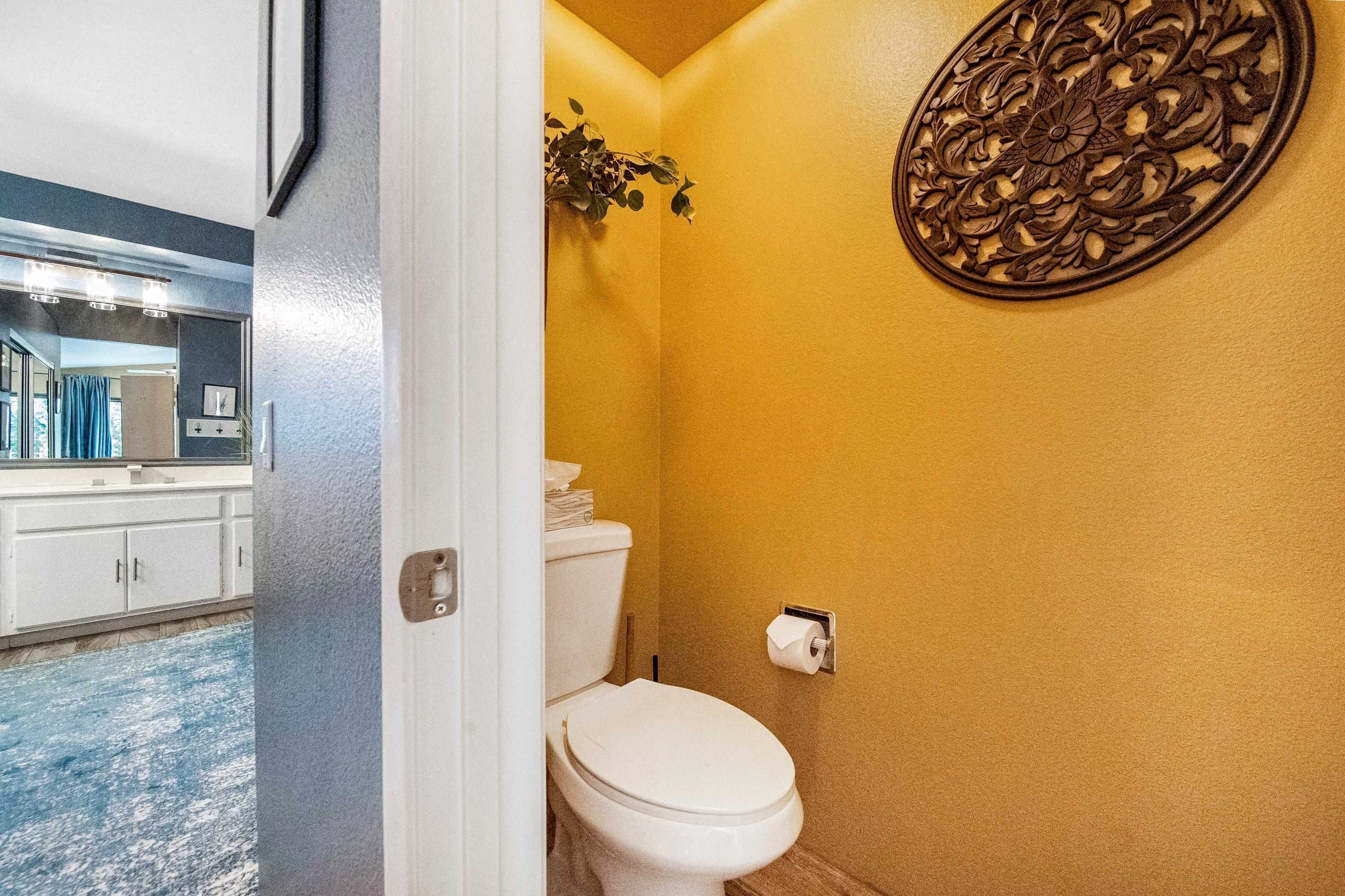 A bathroom with a toilet, a wall-mounted decorative piece, and a visible sink area with cabinets.