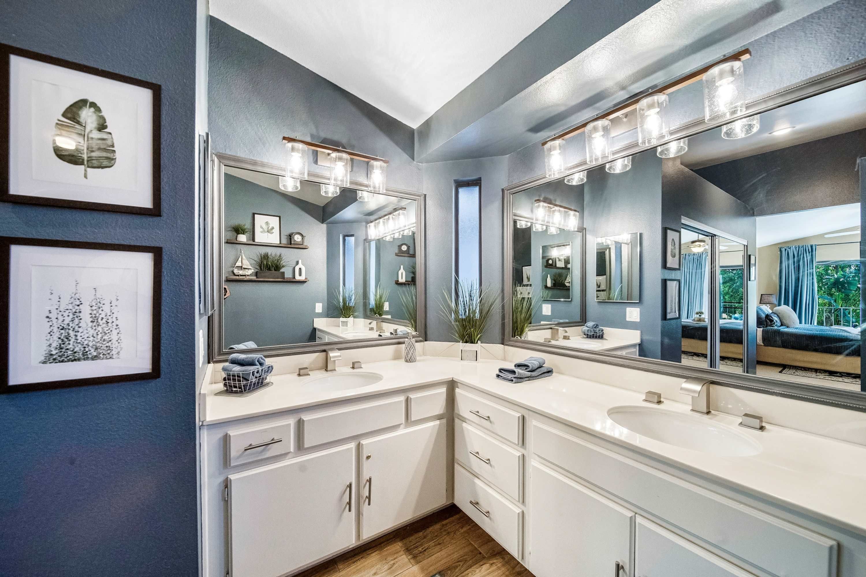 A modern bathroom with two sinks, large mirrors, and framed artwork on the wall.