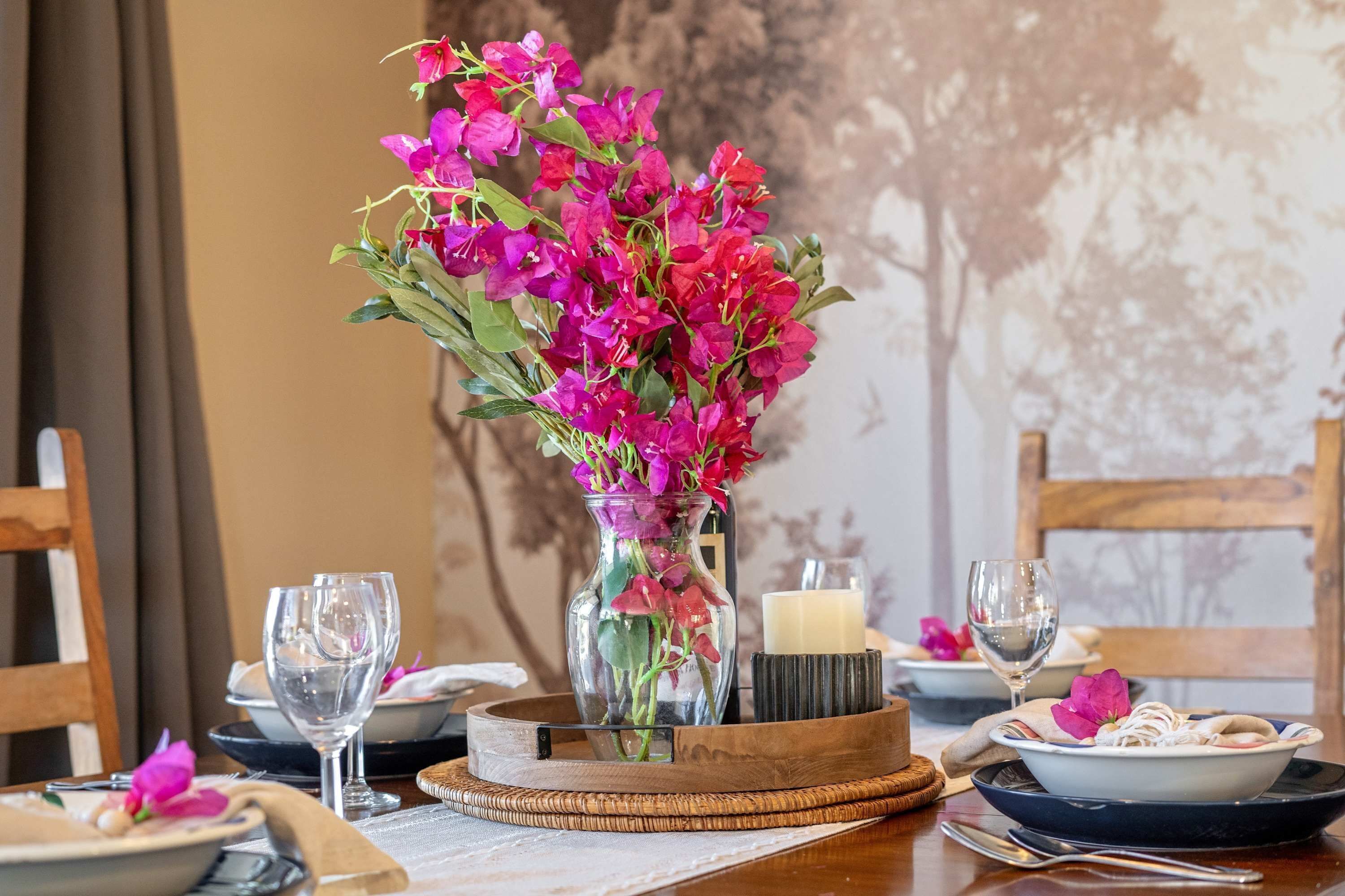 A dining table set with plates, glasses, a vase with flowers, and a candle.