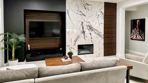 A modern living room with a large flat-screen TV, a fireplace, and a sectional sofa. - Palm Luxe Estate Luxury Desert Retreat With Pool (Indio)