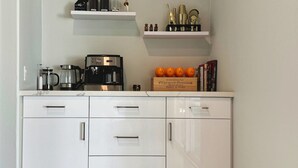 A kitchen with white cabinets, a coffee maker, a kettle, and a wooden box with oranges and champagne bottles. - Palm Luxe Estate Luxury Desert Retreat With Pool (Indio)
