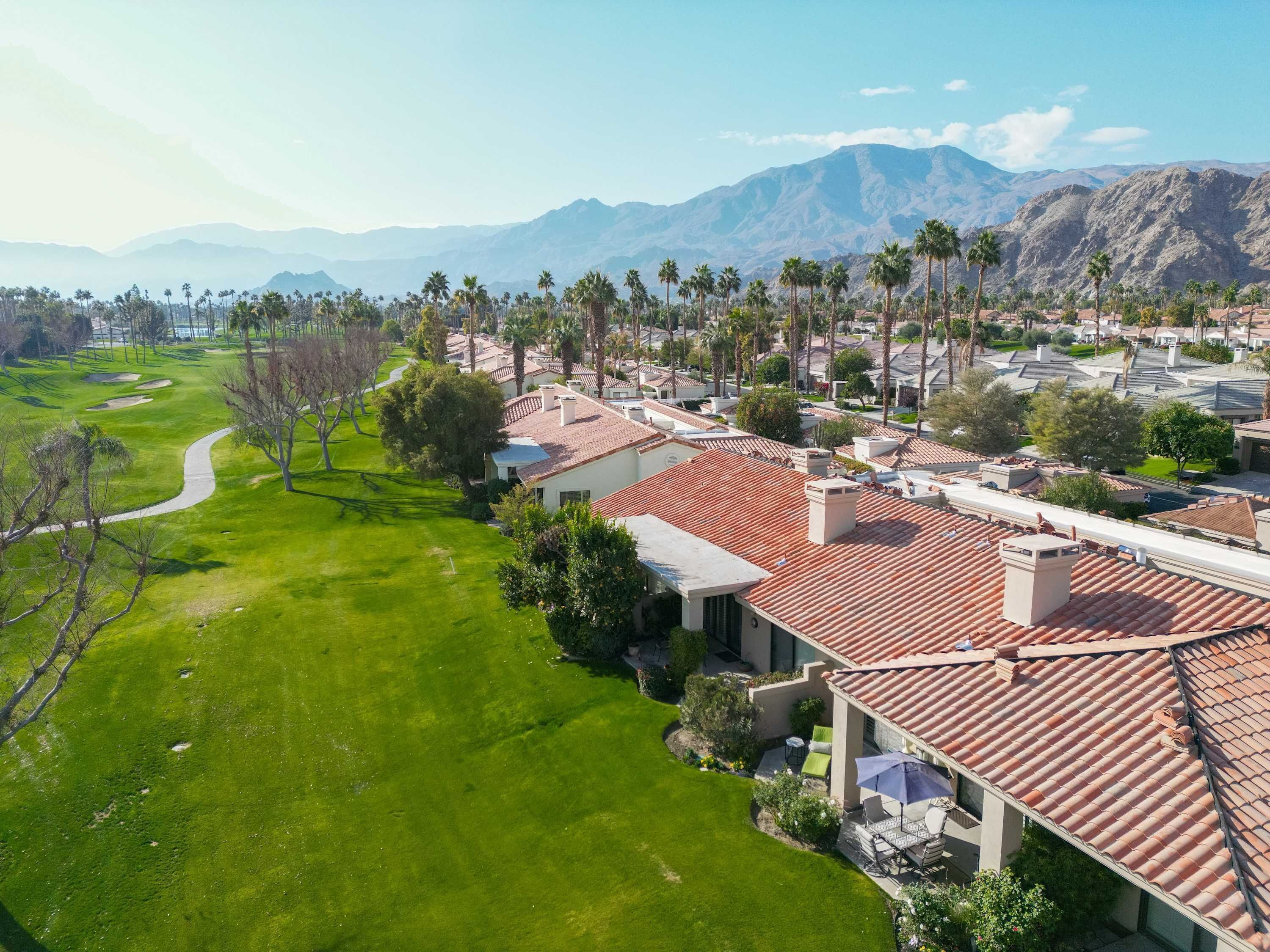 A residential area with houses featuring red-tiled roofs, a well-maintained lawn, and a golf course in the background.