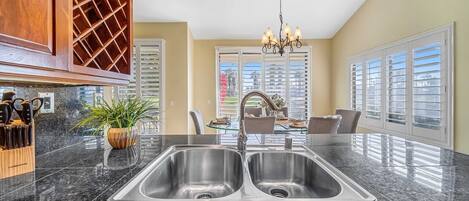 A kitchen with a double sink, wooden cabinets, a wine rack, and a dining area with a chandelier.