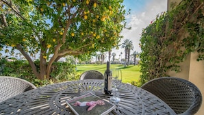 An outdoor dining area with wicker chairs and a table, a bottle of wine, and a magazine.