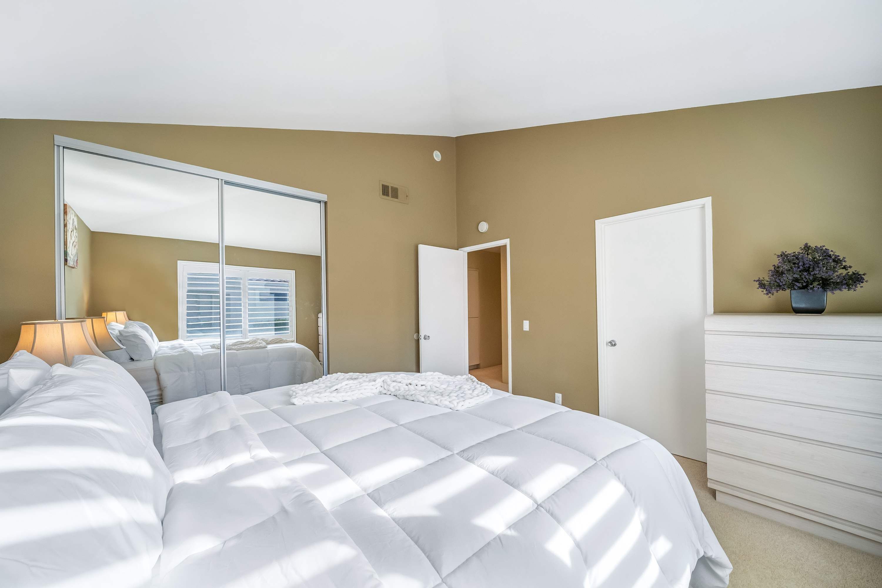 Un dormitorio con una cama grande, un aparador, un espejo y una puerta que da a otra habitación.