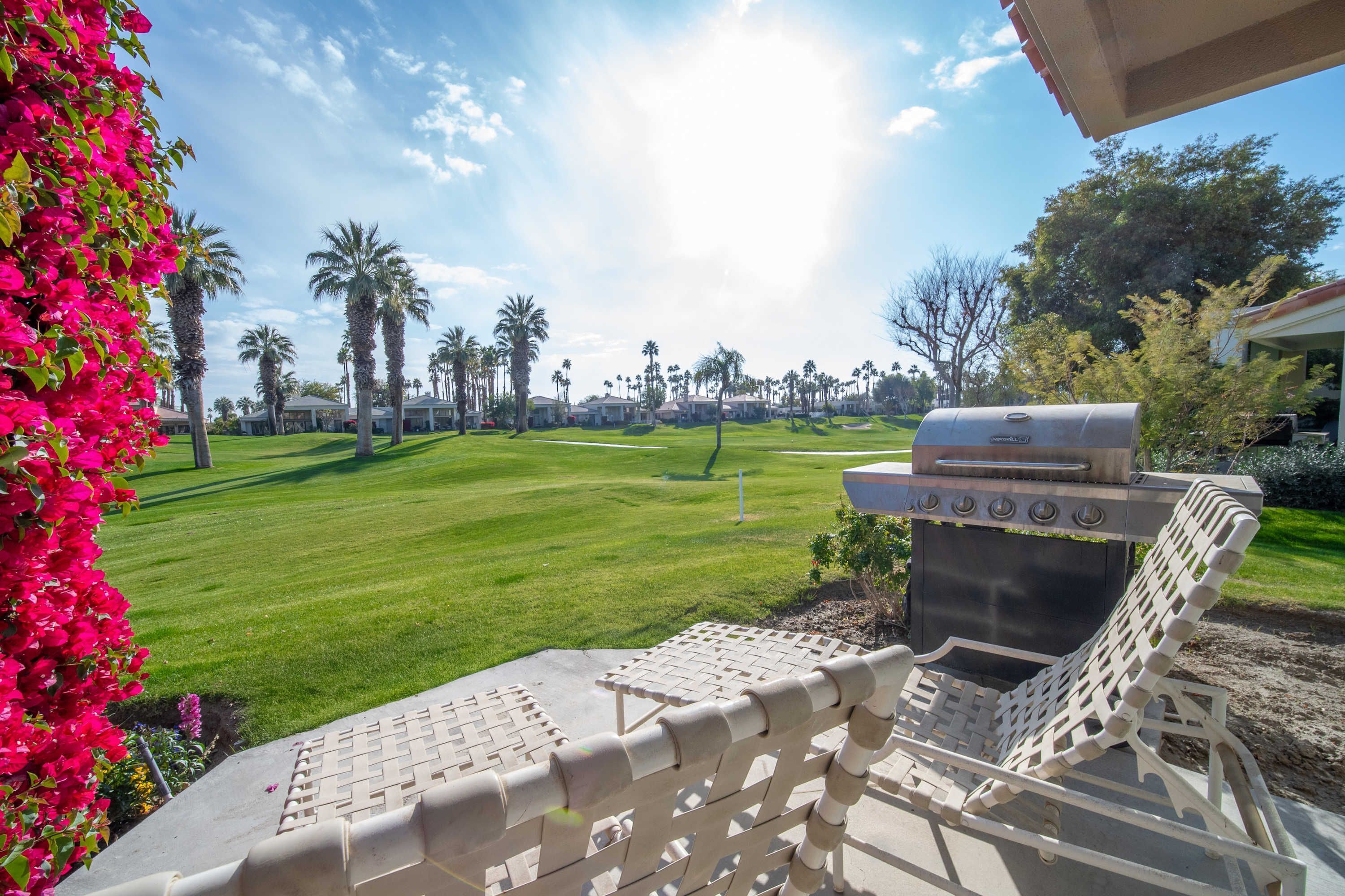 A patio with a grill and lounge chairs overlooking a golf course.
