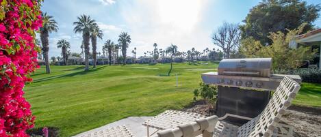 A patio with a grill and lounge chairs overlooking a golf course.