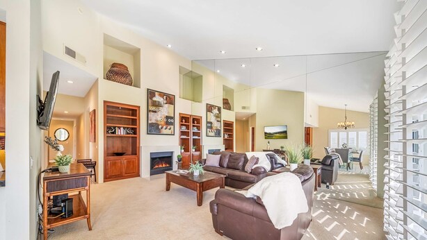 A spacious living room with a fireplace, a sofa, a coffee table, and a TV mounted on the wall.