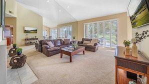 A spacious living room with two leather sofas, a coffee table, and a TV mounted on the wall.