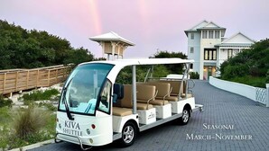 A white beach shuttle with a canopy, labeled "KIVA SHUTTLE," parked on a paved path with a beach house in the background. - Gulf Shores Hideaway Walk to Waves Pool Golf Views (Gulf Shores)