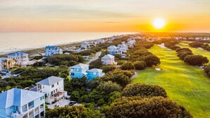 A coastal residential area with houses, a golf course, and a sunset over the ocean. - Gulf Shores Hideaway Walk to Waves Pool Golf Views (Gulf Shores)