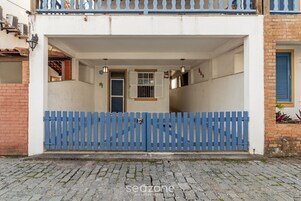Um edifício com portão azul, placa com o número 27 e fachada branca.