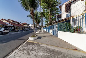 Rua com edifícios, calçada e cerca azul.