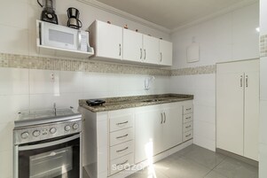 Uma cozinha com armários brancos, micro-ondas, cafeteira e fogão.
