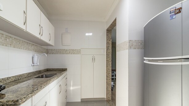 Una cocina moderna con armarios blancos, encimera de granito y refrigerador integrado.