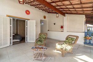 Uma sala de estar integrada com móveis de vime, uma mesinha com objetos decorativos e vista para o exterior.