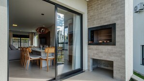 Un espace de repas extérieur moderne, doté d’une porte vitrée donnant sur un salon, d’une cheminée en briques et d’un ventilateur de plafond.