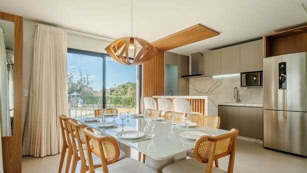 Une cuisine moderne dotée d’un réfrigérateur en acier inoxydable, un coin repas avec une table en verre et des chaises en bois, et une vue sur l’extérieur.