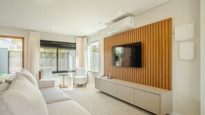 Un salon moderne avec un téléviseur à écran plat fixé sur un mur recouvert de panneaux en bois, un canapé, une table basse et une table d’appoint.
