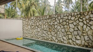 Una piscina con pared de piedra y borde de azulejos, rodeada de palmeras.