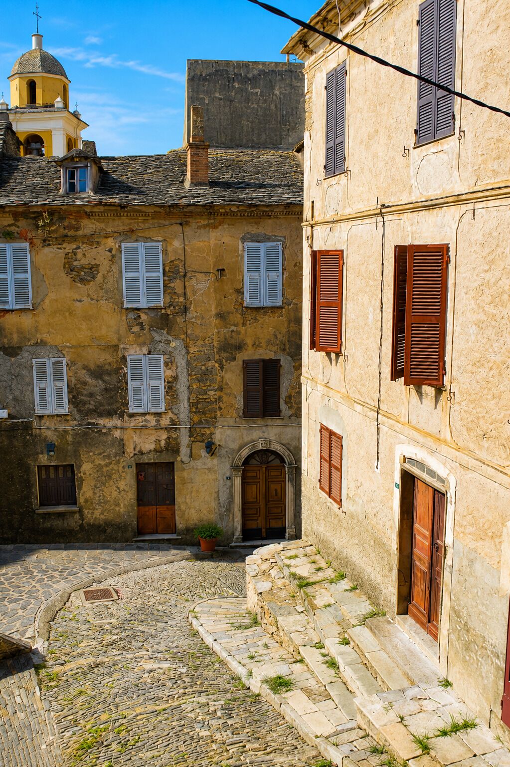 Une ruelle étroite pavée, bordée de vieux bâtiments aux portes cintrées et aux fenêtres à volets.