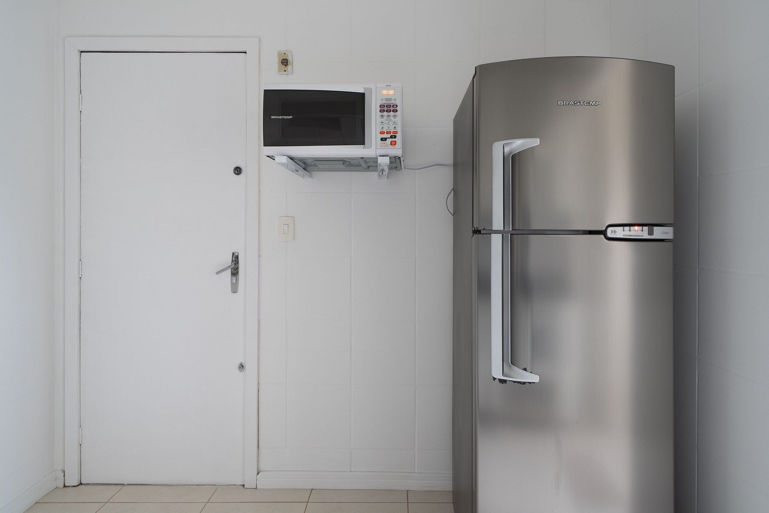 Ett kylskåp i rostfritt stål med en digital kontrollpanel, en mikrovågsugn placerad ovanför och en vit dörr.